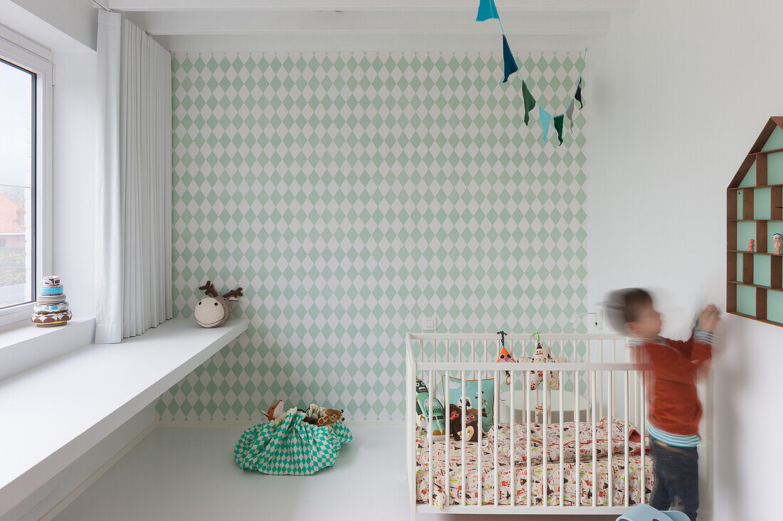 Children's room with green and white wallpaper, wall shelves and white crib