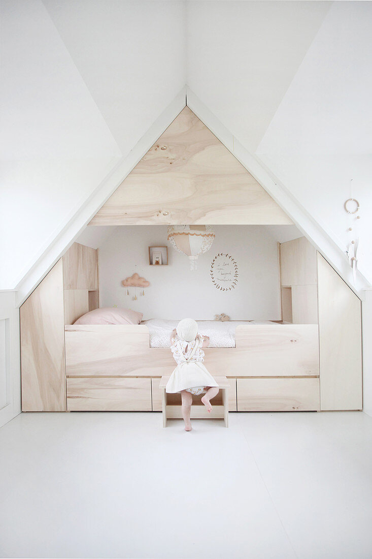 Child climbing into modern cubby bed surrounded by storage in attic bedroom