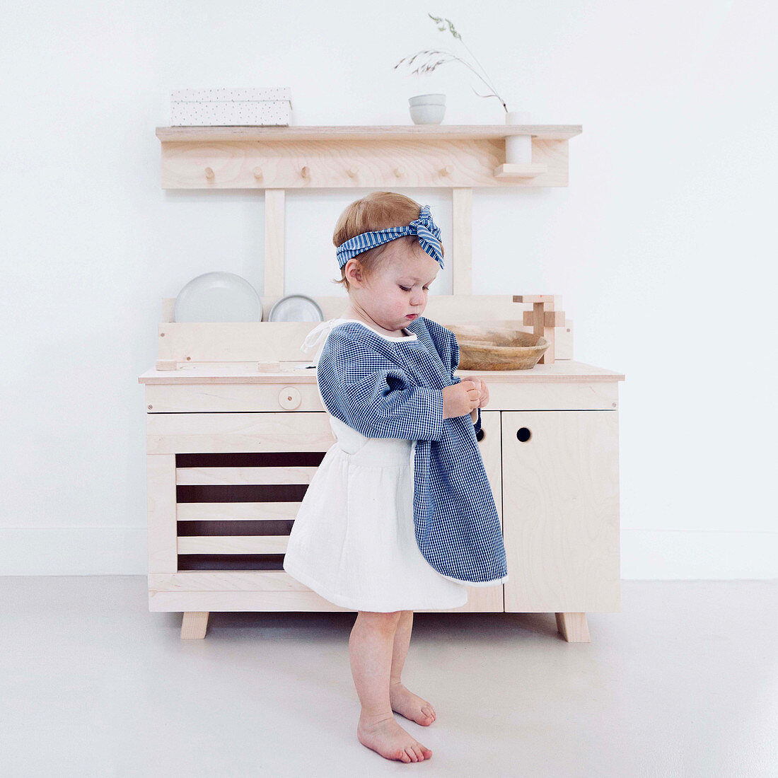 Little girl standing in front of pale wooden play kitchen