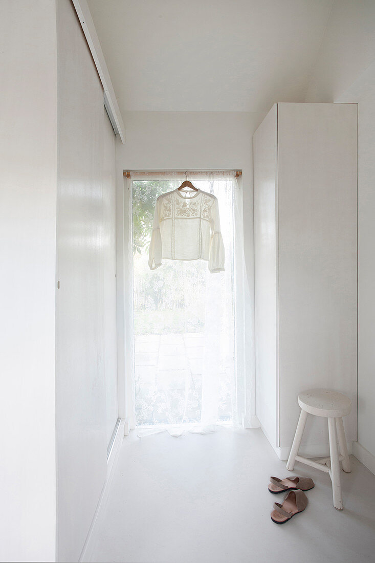 Romantische Bluse hängt im Fenster mit Gardine im weißen Raum