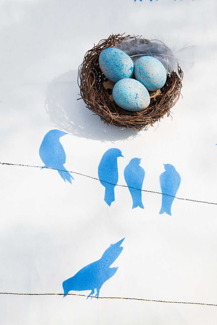 Osternest mit blau gefärbten Eiern auf Tischdecke mit Vogelmotiven in Schablonentechnik