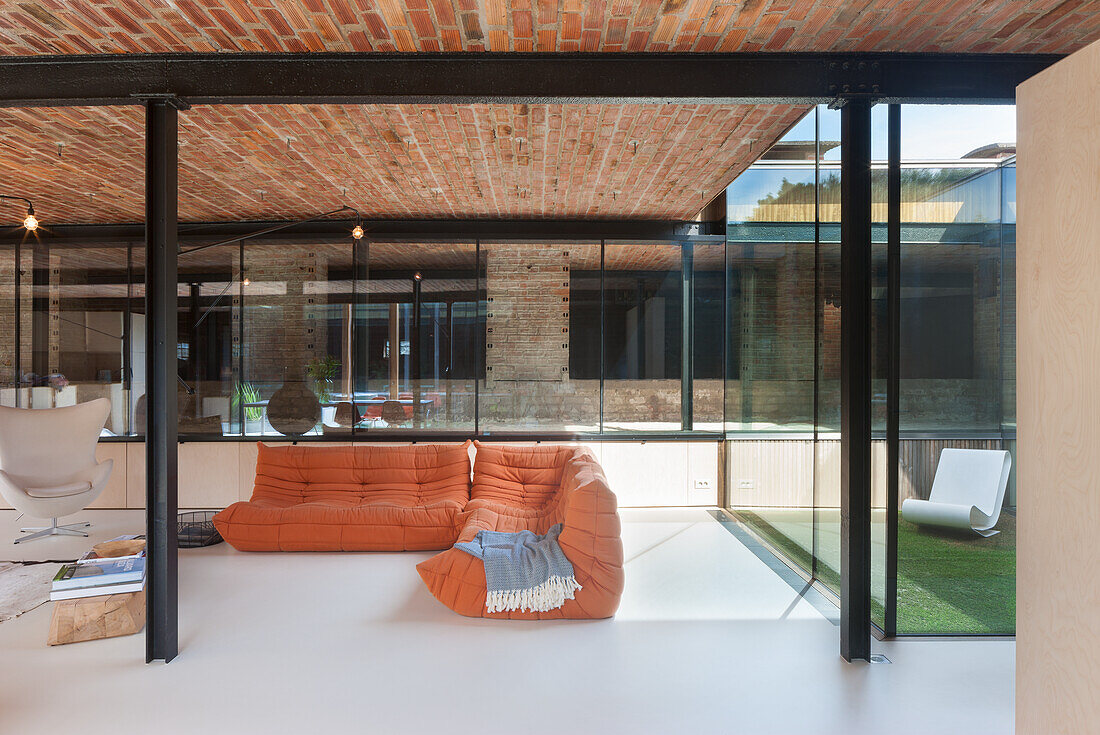 Open-plan living area with orange sofa and tiled ceiling and glass walls