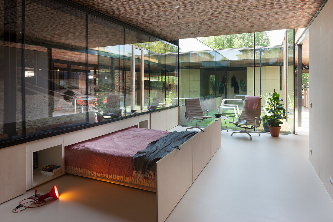 Pull-out bed in guest room in front of glass wall with view of inner courtyard