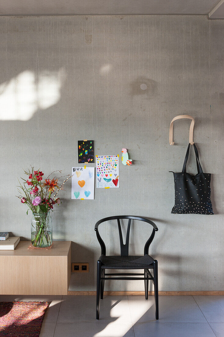 Exposed concrete wall with children's drawings, black wooden chair and sideboard