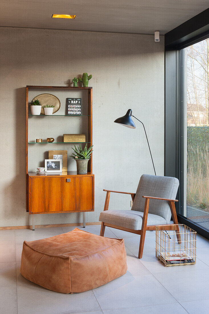 Vintage Sideboard aus Holz neben modernem Sessel mit Leseleuchte und Pouf