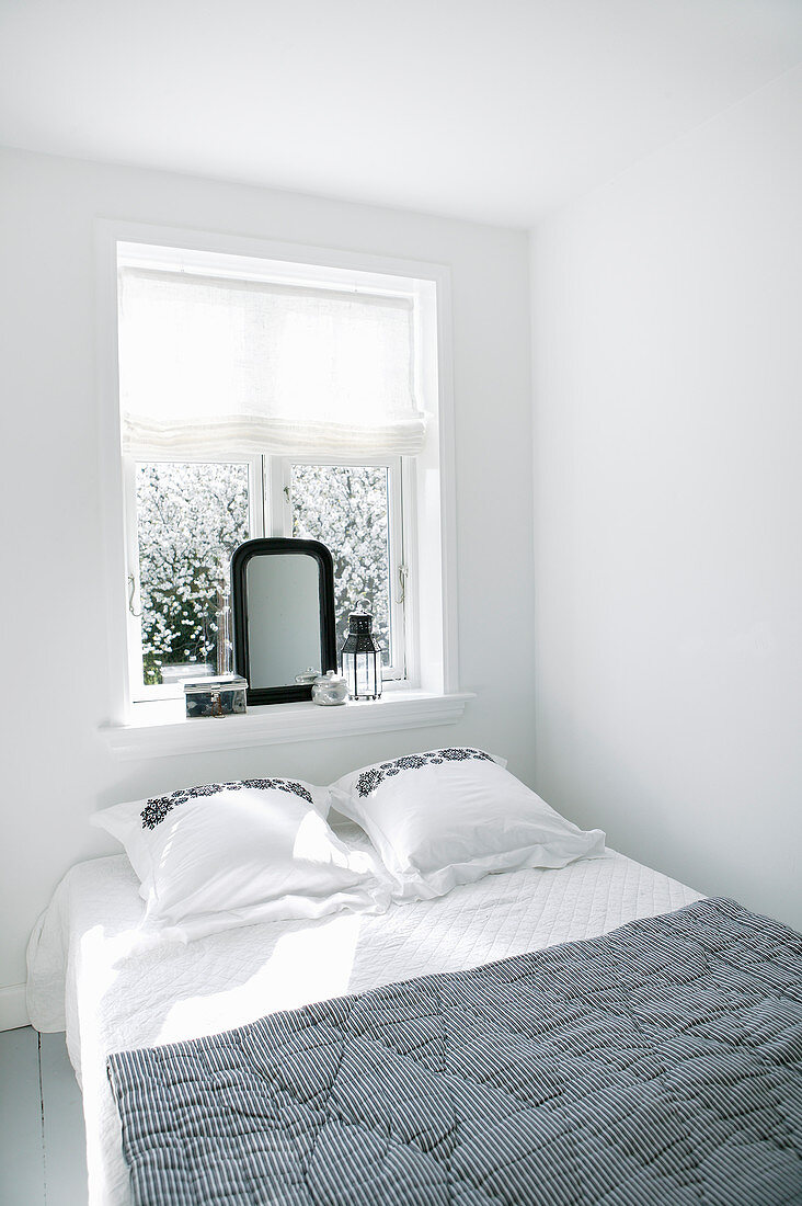 Bett vorm Fenster im schlichten Schlafzimmer in Weiß