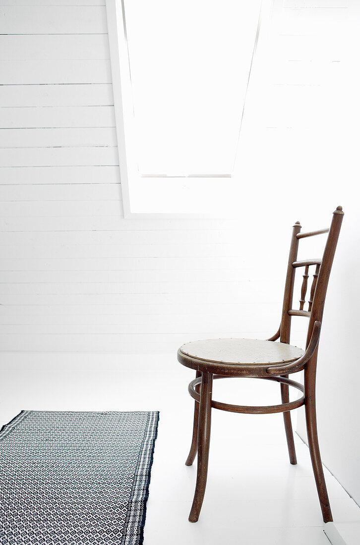 Alter Stuhl auf weißem Boden unterm Dachfenster