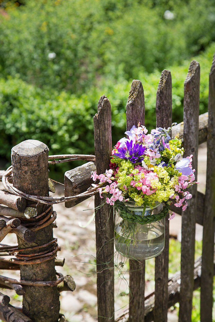Summer bouquet in preserving jar tied to garden fence