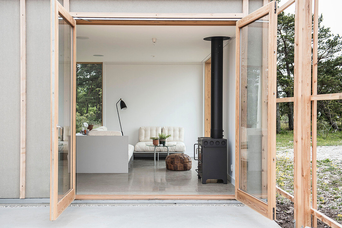 View through open terrace doors into simple living room with wood-burning stove