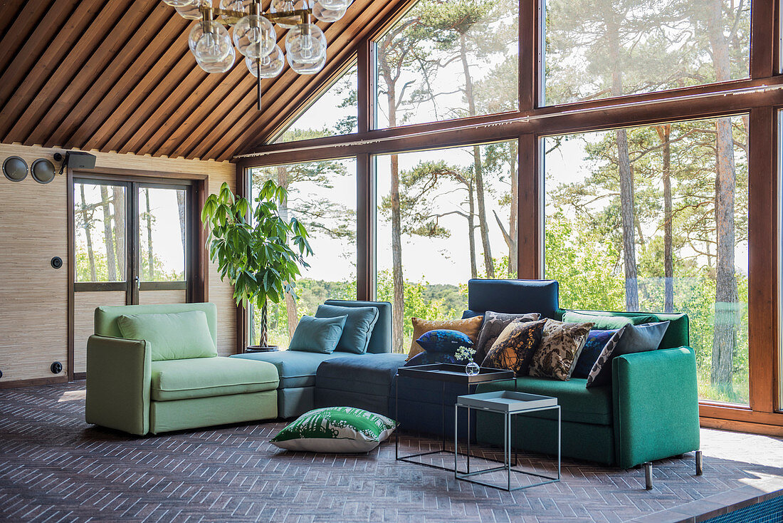 Sofa aus verschiedenen Elementen in Grün und Blau vor Fensterfront