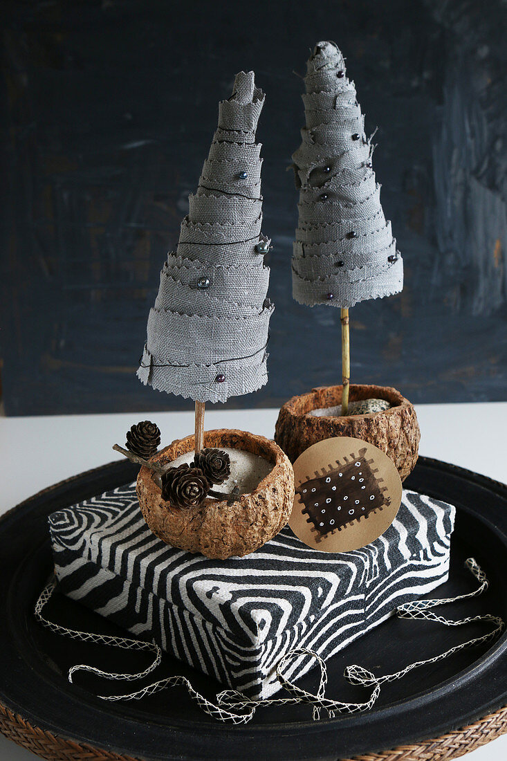 Two miniature fabric fir trees on zebra-patterned box against black background