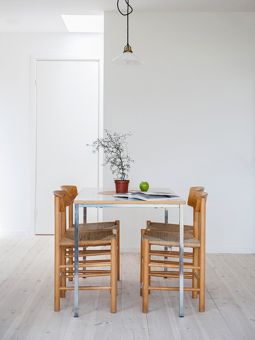 Slender dining table with four chairs in front of white wall