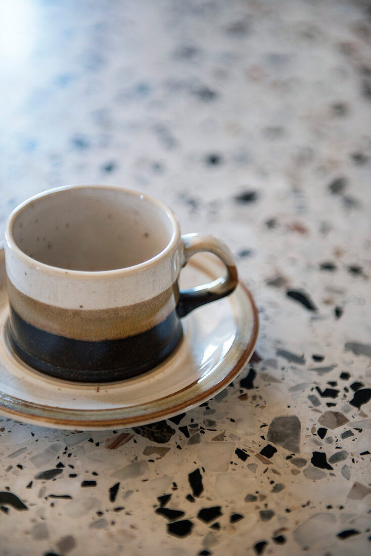 Three-coloured stoneware cup and saucer on terrazzo surface