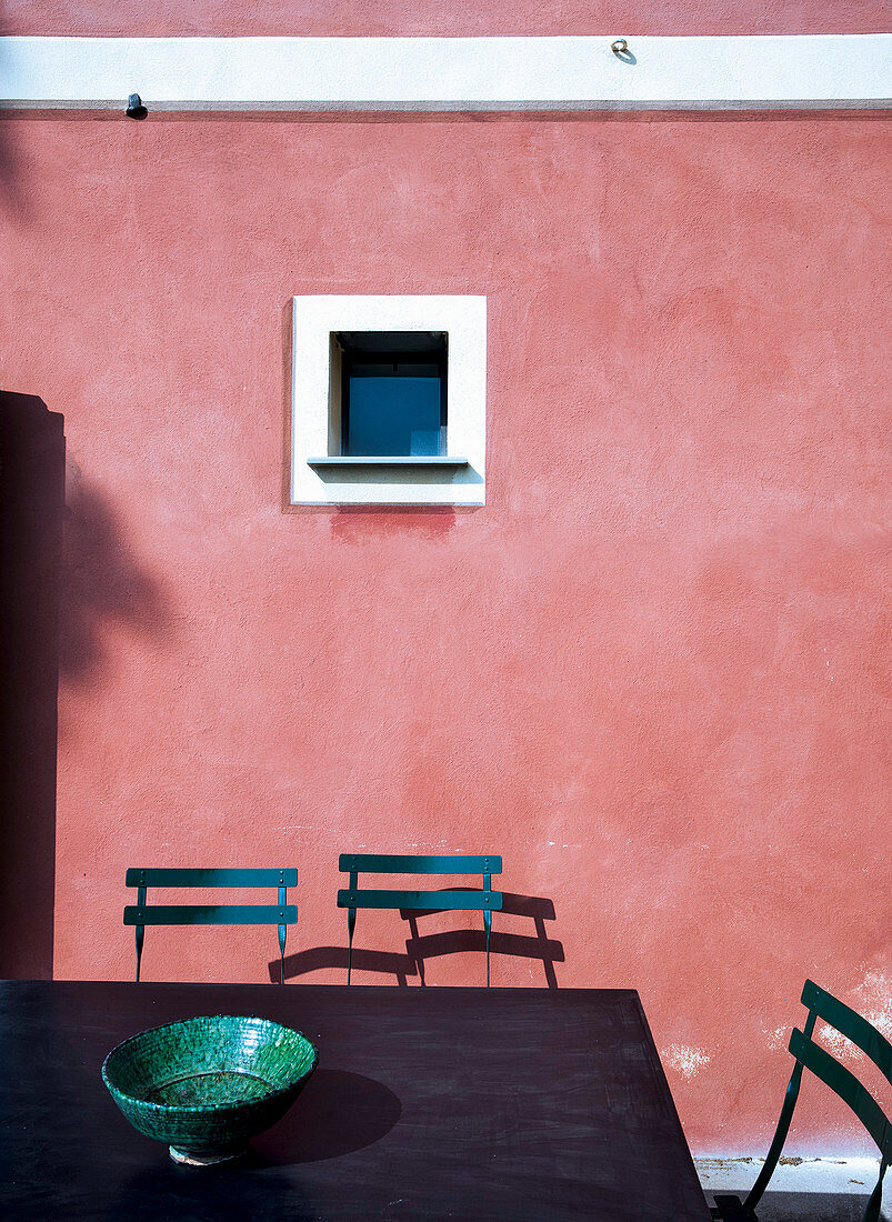 Table and chair in front of small window in pink façade