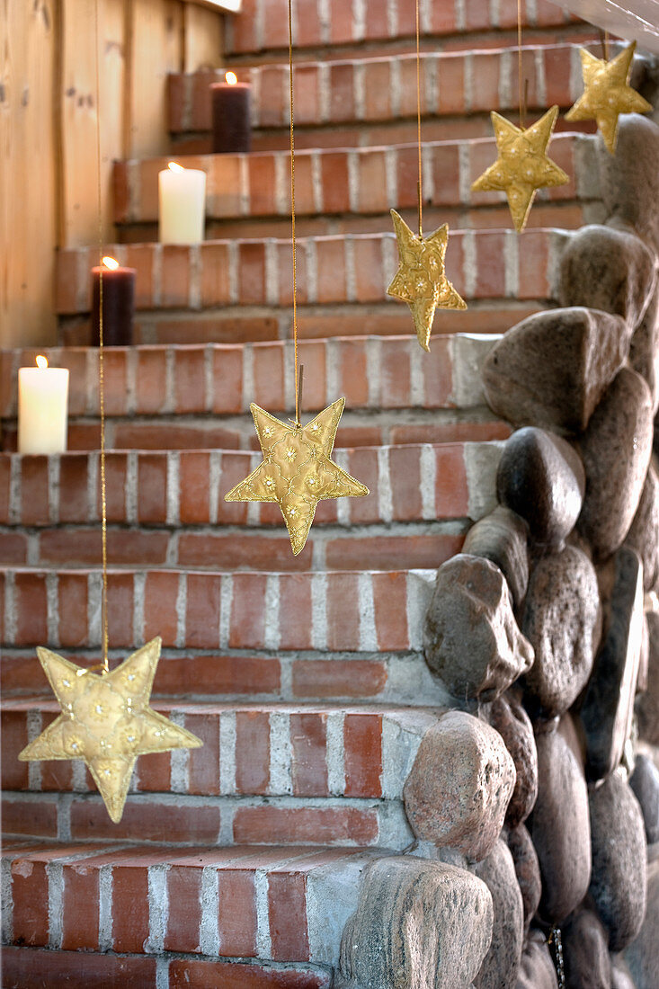 Stumpenkerzen und goldene Sterne als weihnachtliche Treppendekoration