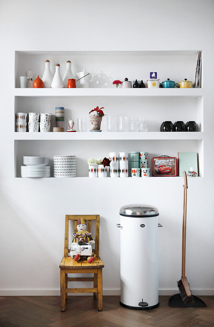 Crockery and kitchen utensils on fitted shelves in niche in white wall