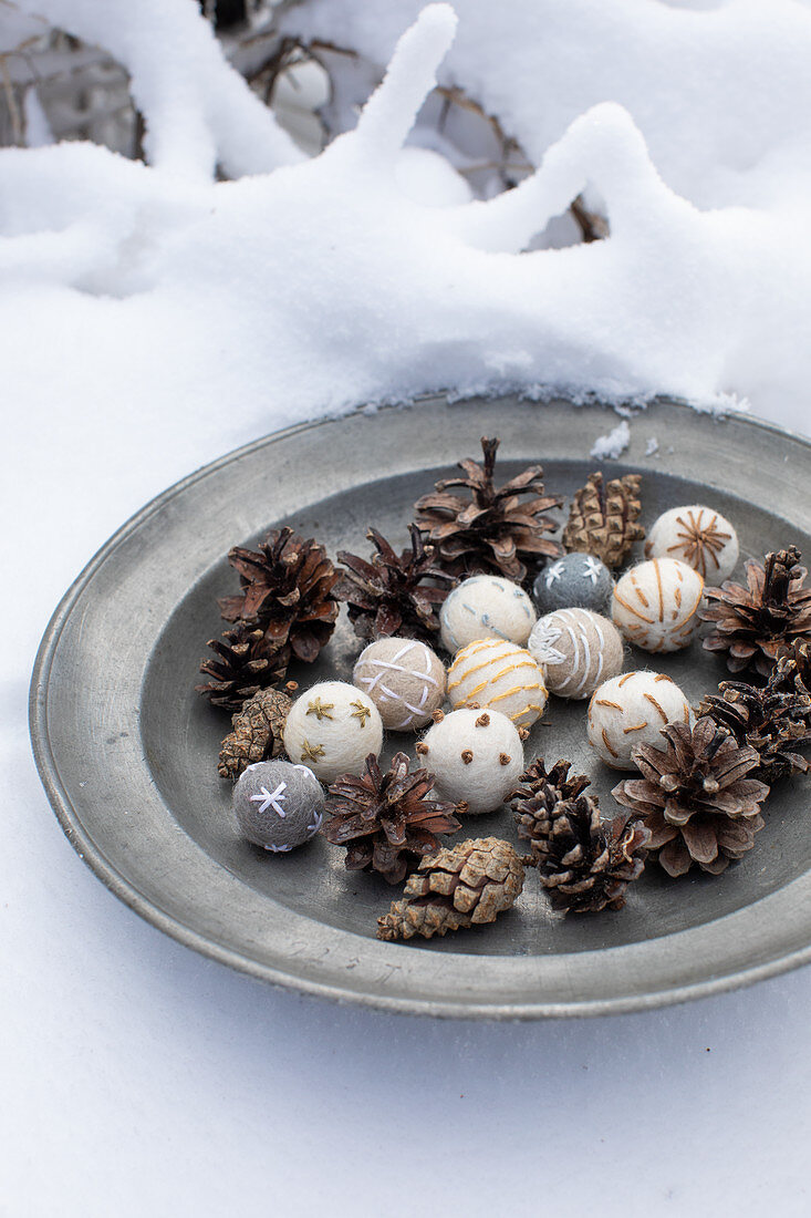 Winterliche Dekoration aus bestickten Filzkugeln und Zapfen