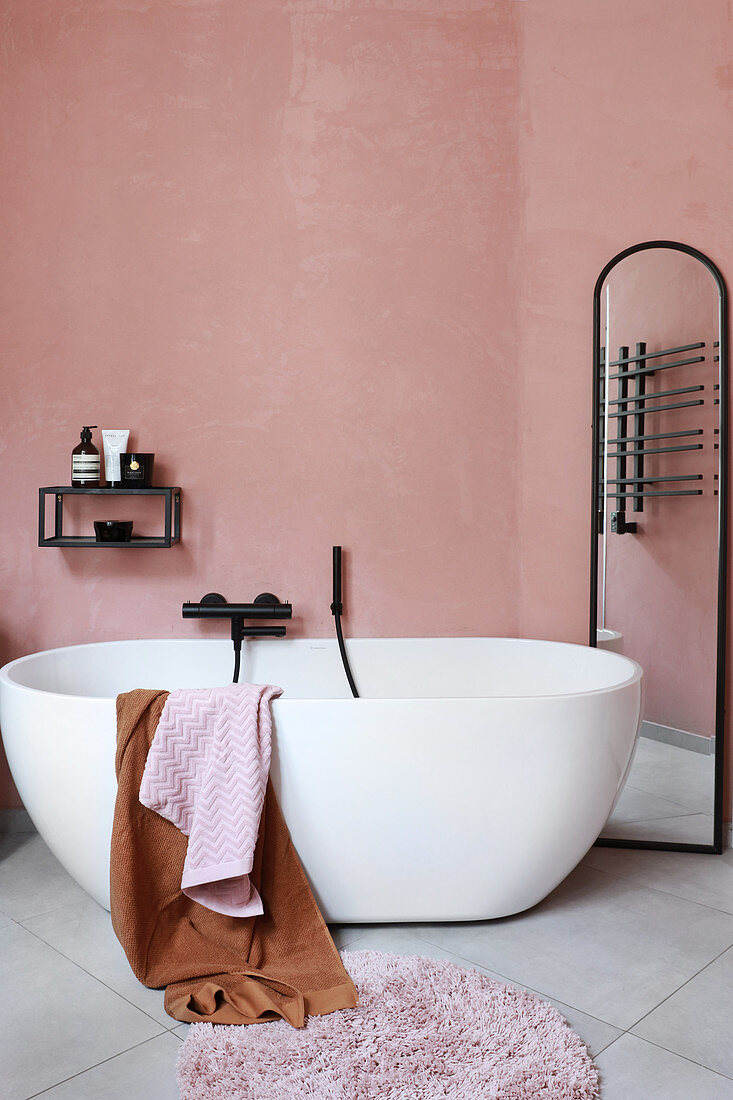 Oval, free-standing bathtub and full-length mirror in pink bathroom