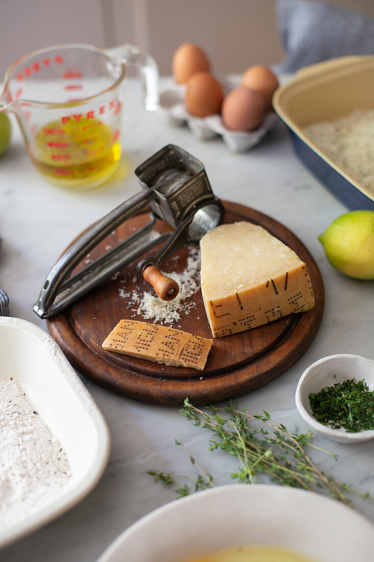 Parmesan cheese and vintage grater on wooden board surrounded by other ingredients