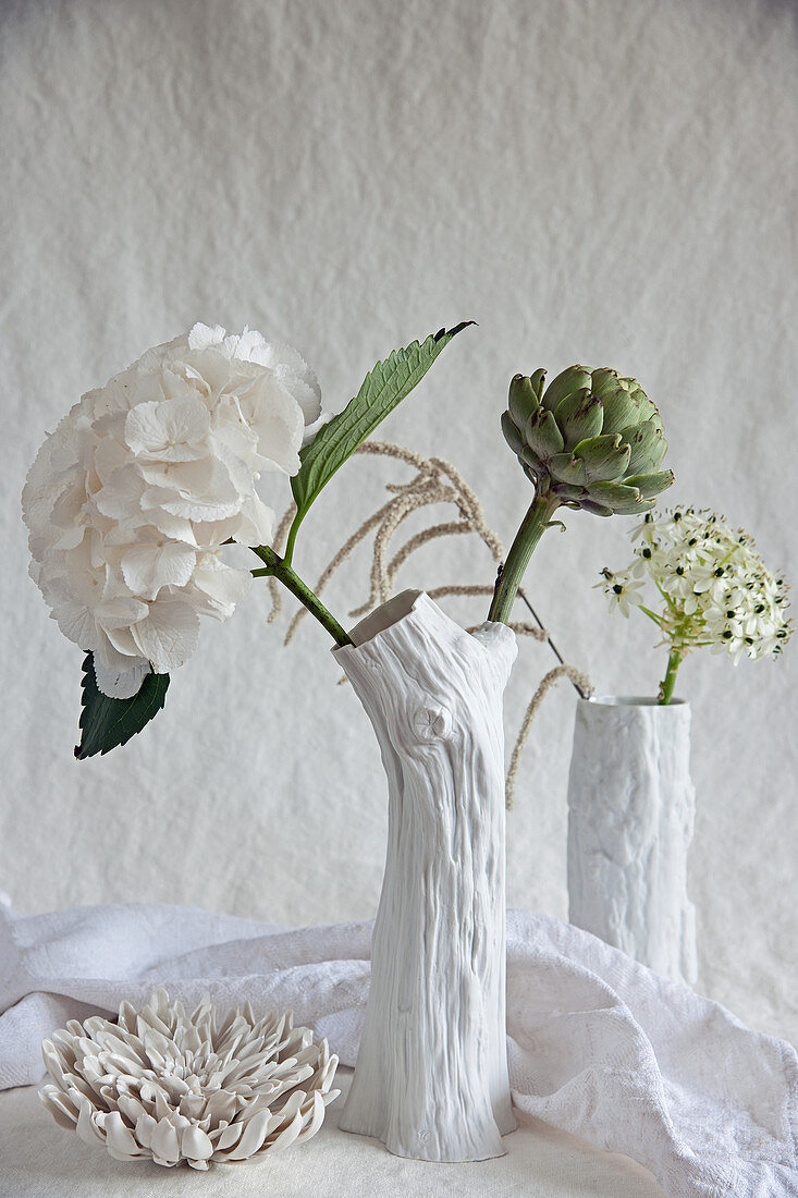 Hortensienblüte, Artischocke, Milchstern und Fuchsschwanz in weißen Vasen