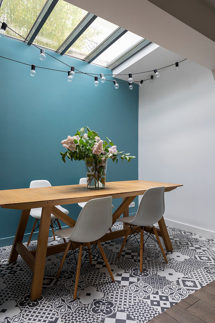Schalenstühle am Holztisch vor blauer Wand auf Musterfliesenboden