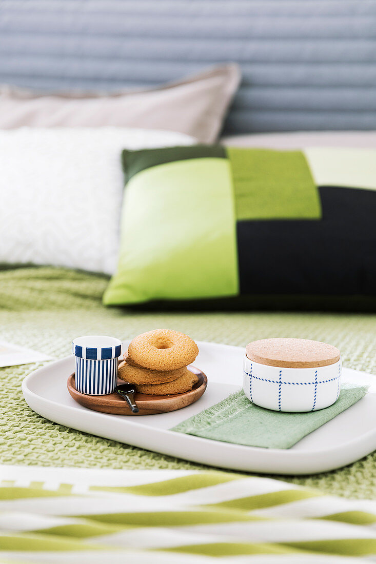 Biscuits and cup of espresso on tray on bed with green bed linen
