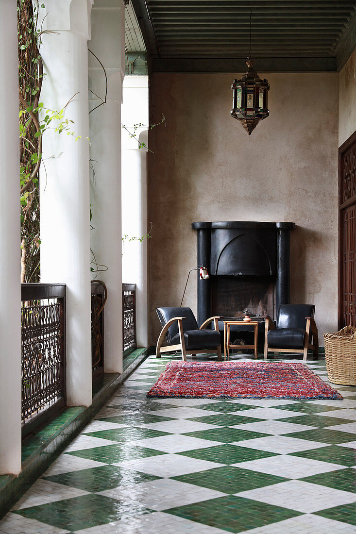Armchairs in front of open fireplace in loggia with chequered floor