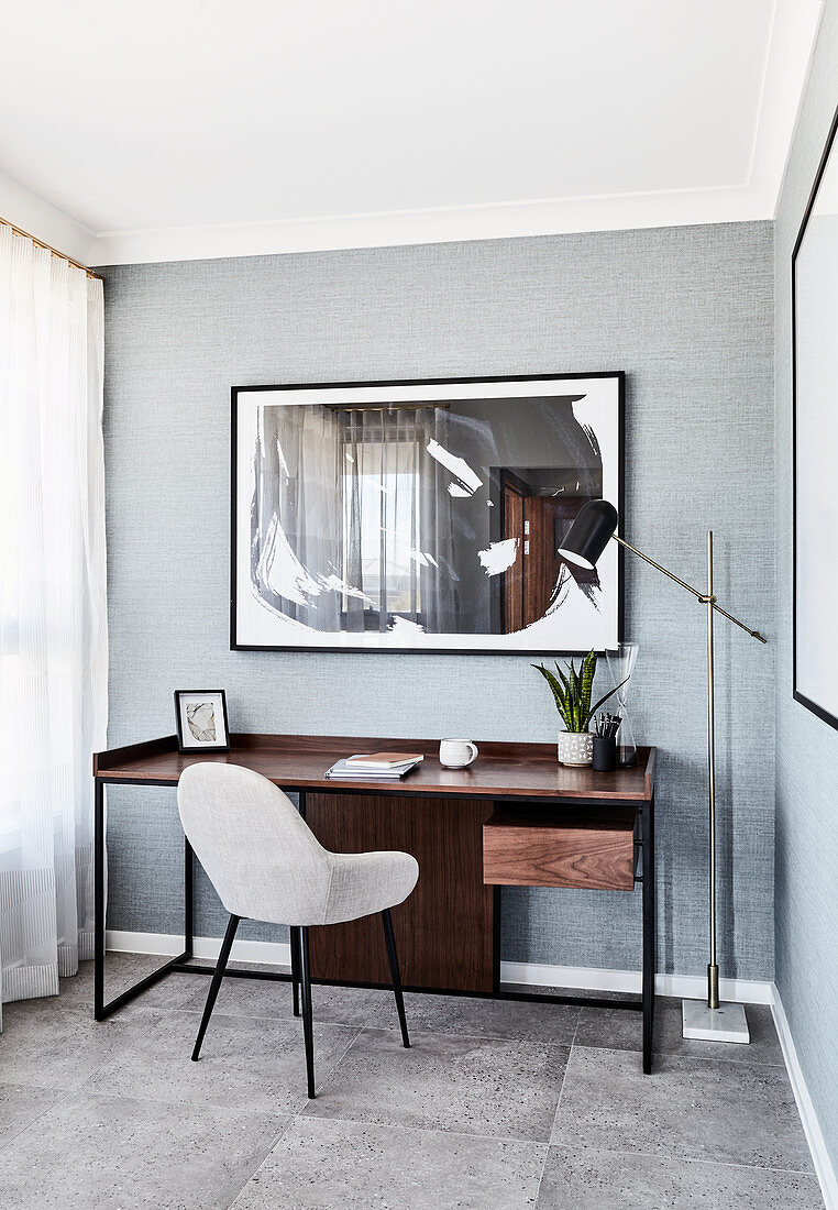 Dark wooden desk and pale upholstered chair in study with grey carpet