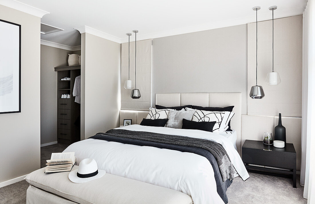 Double bed with tall headboard, pendant lamps above bedside tables and view into dressing area in elegant bedroom
