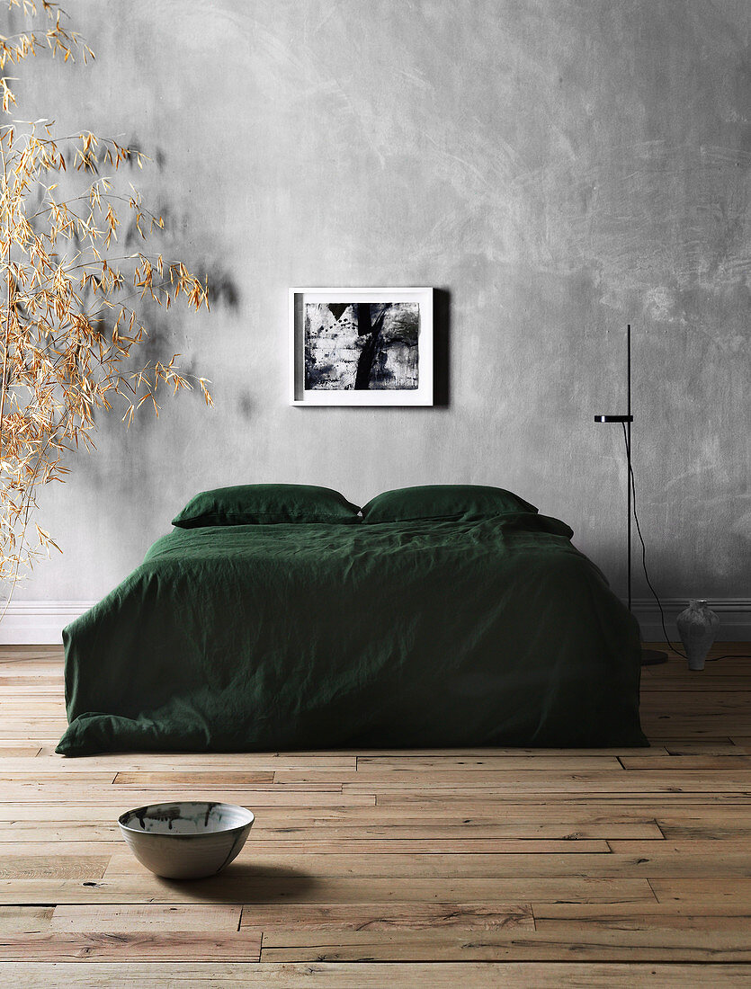 Doppelbett mit grüner Tagesdecke und Stehleuchte vor grauer Wand