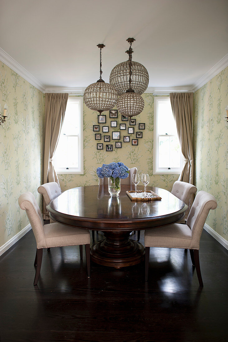 Anitker, ovaler Esstisch mit hellen Polsterstühlen und Hängelampen im Esszimmer mit Tapete