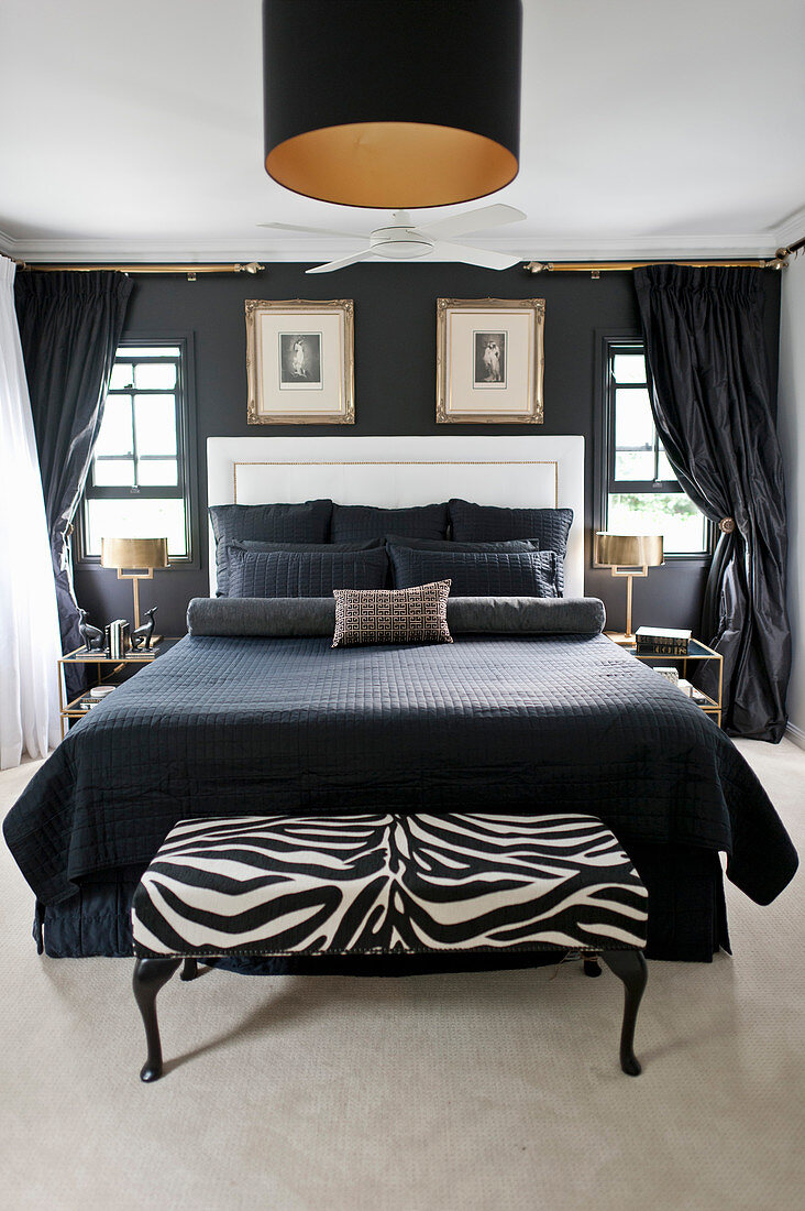 Doppelbett mit schwarzen Accessoires und weißem Betthaupt im Schlafzimmer mit schwarzer Wand, Kleiderbank in Zebra-Look