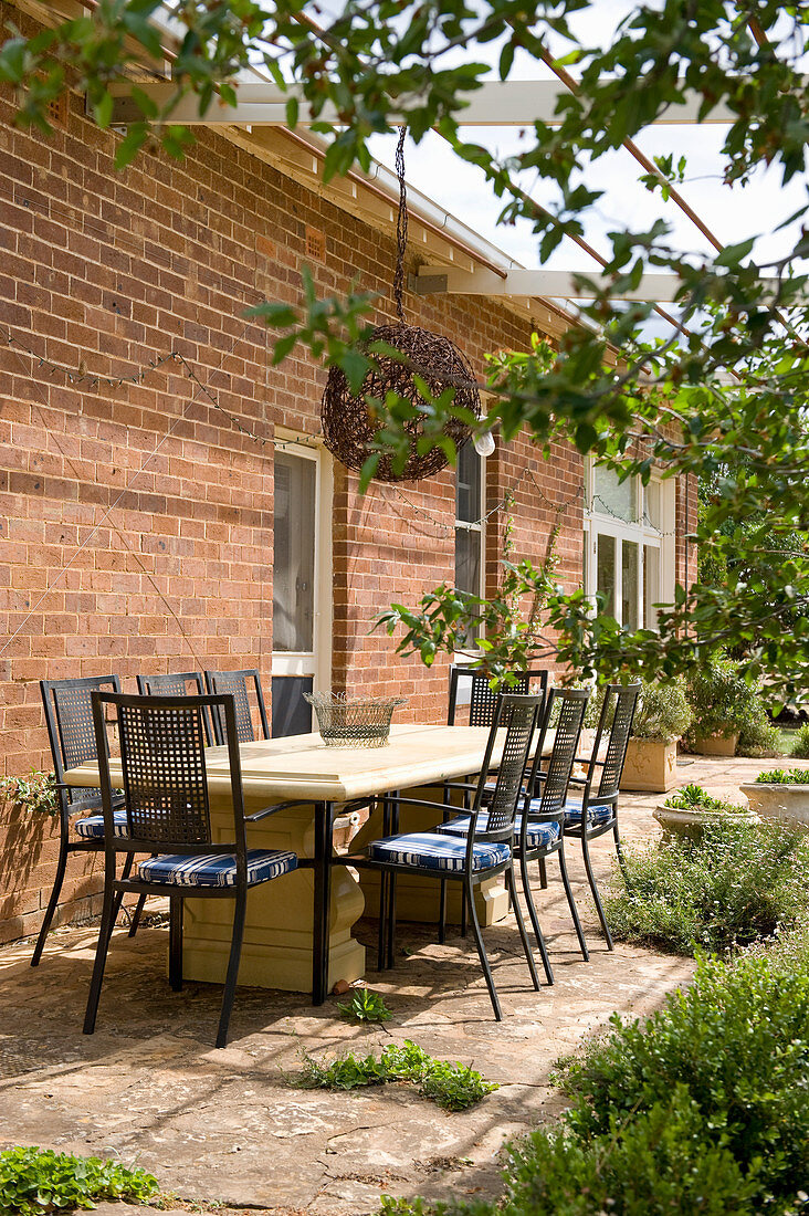 Solid wooden table and black metal chairs on veranda outside brick house