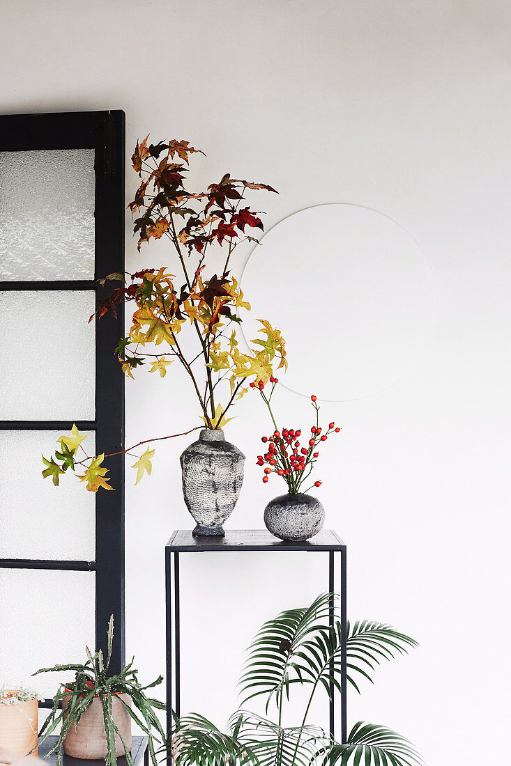 Branches with autumn leaves and rose hips in vases