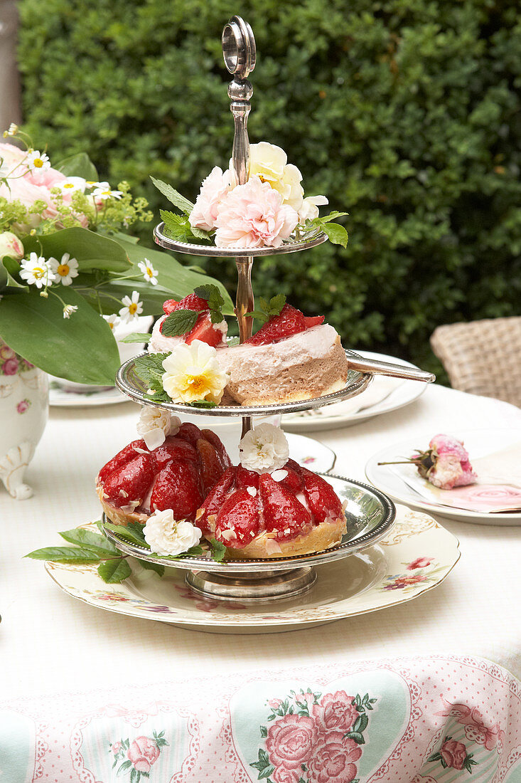 Silberne Etagere mit Rosenblüten und Erdbeerkuchen als Tischdekoration