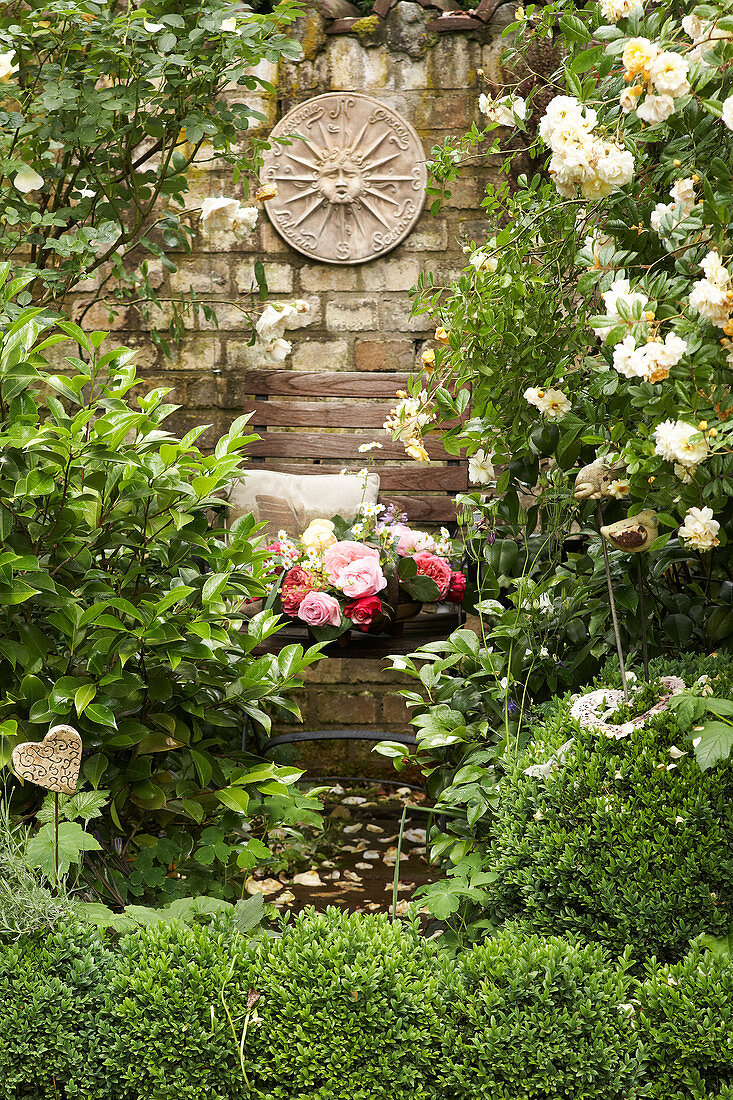 Basket of roses on garden chair next to climbing rose and wall in sunshine