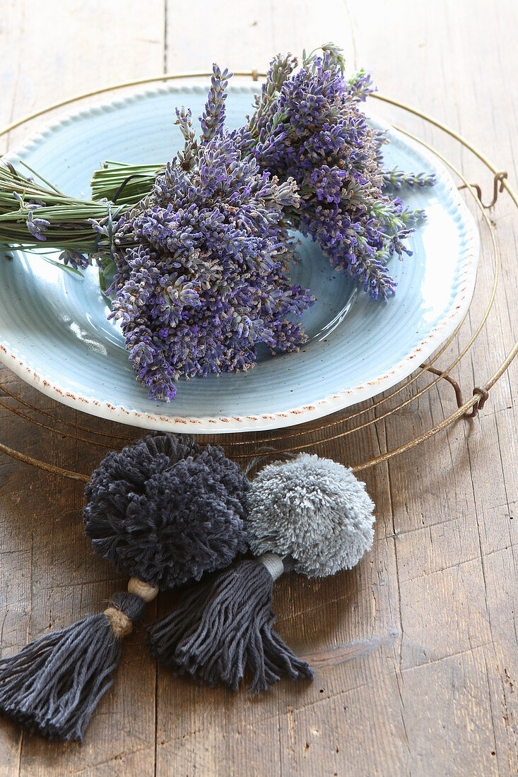 Lavendelsträußchen auf Telller davor zwei Pompoms mit Quasten