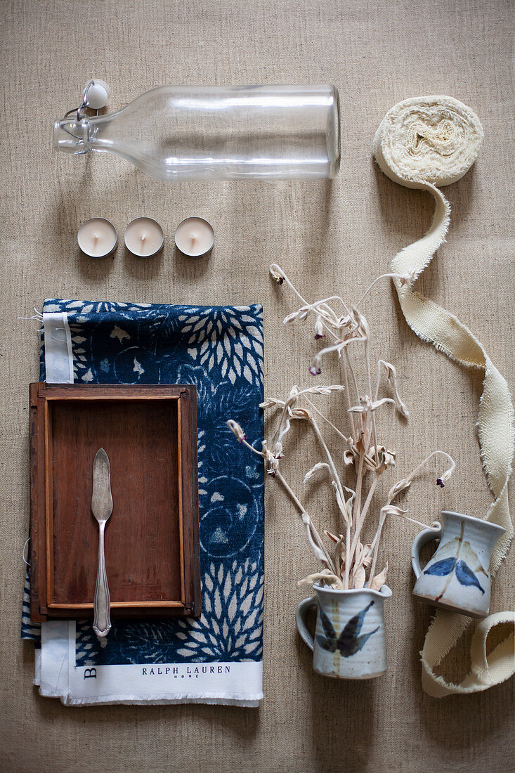 Bügelflasche, Teelichter, Stoffband, Kännchen mit Trockenzweig und Fischmesser auf Holzschale