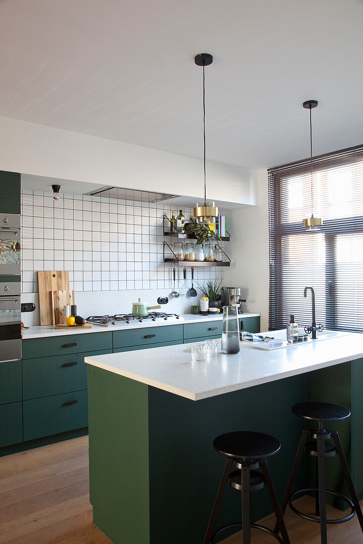 Barstools at island counter in kitchen with dark green cupboards