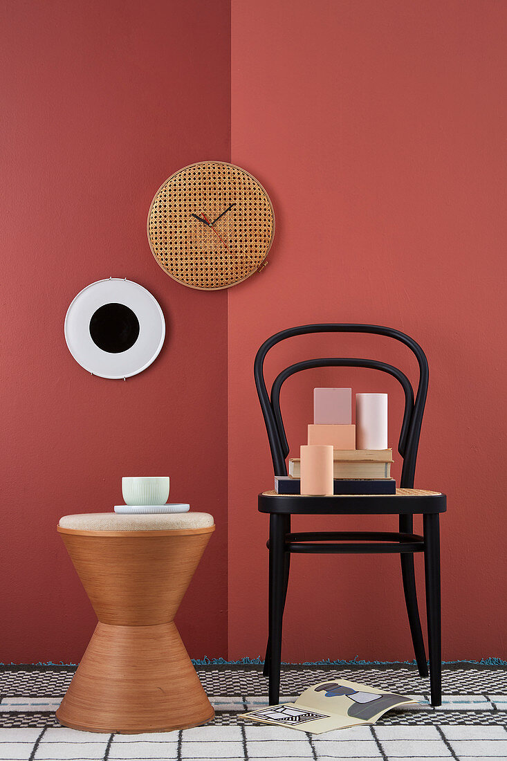 DIY-Wanduhr aus Wiener Geflecht an rot gestrichener Wand, Stuhl mit Dekoobjekten und Beistelltisch