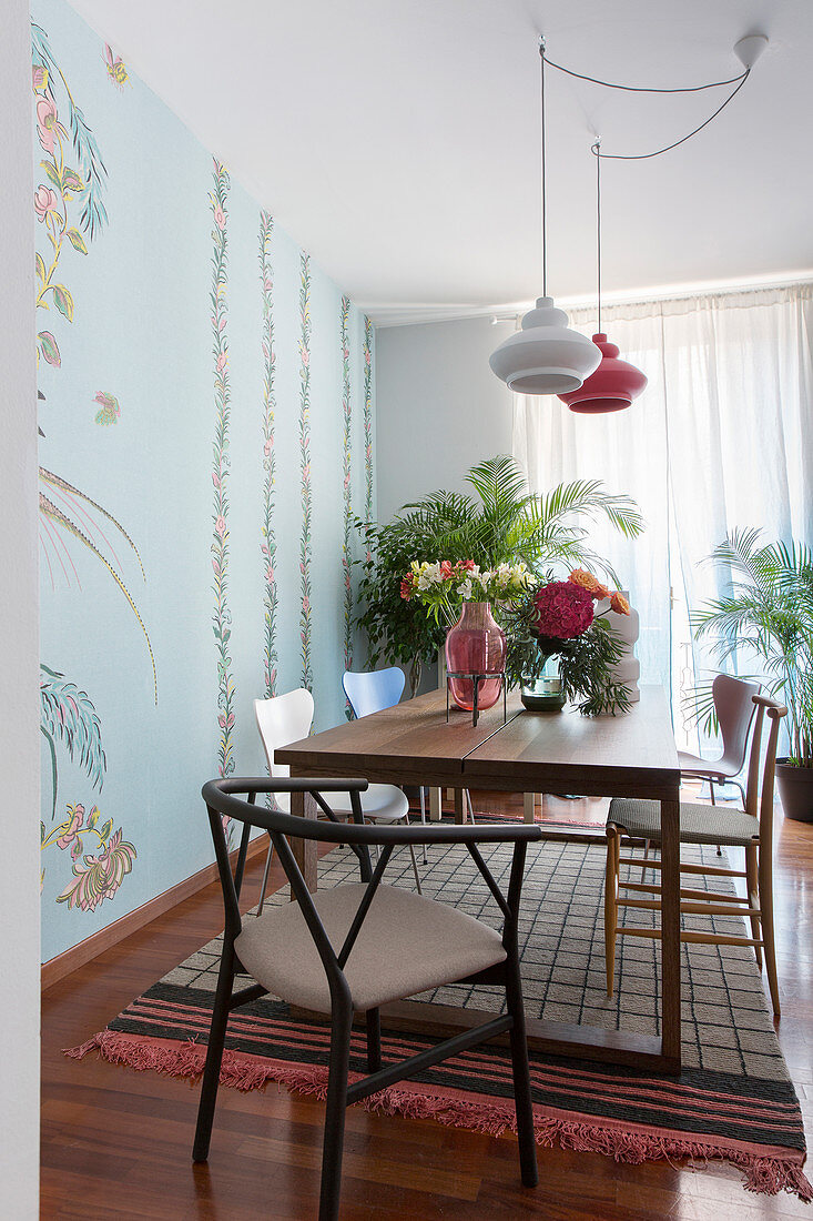 Various chairs around dining table next to floral wallpaper