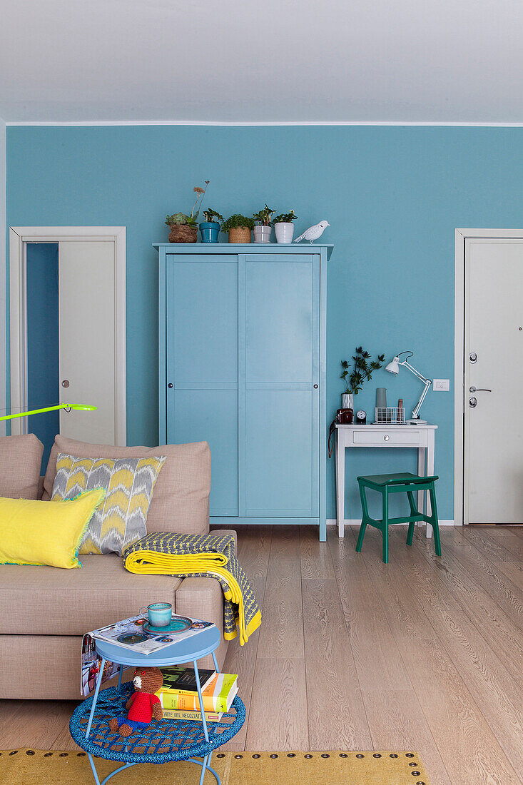 Blue cupboard against blue wall in living room with beige sofa in foreground