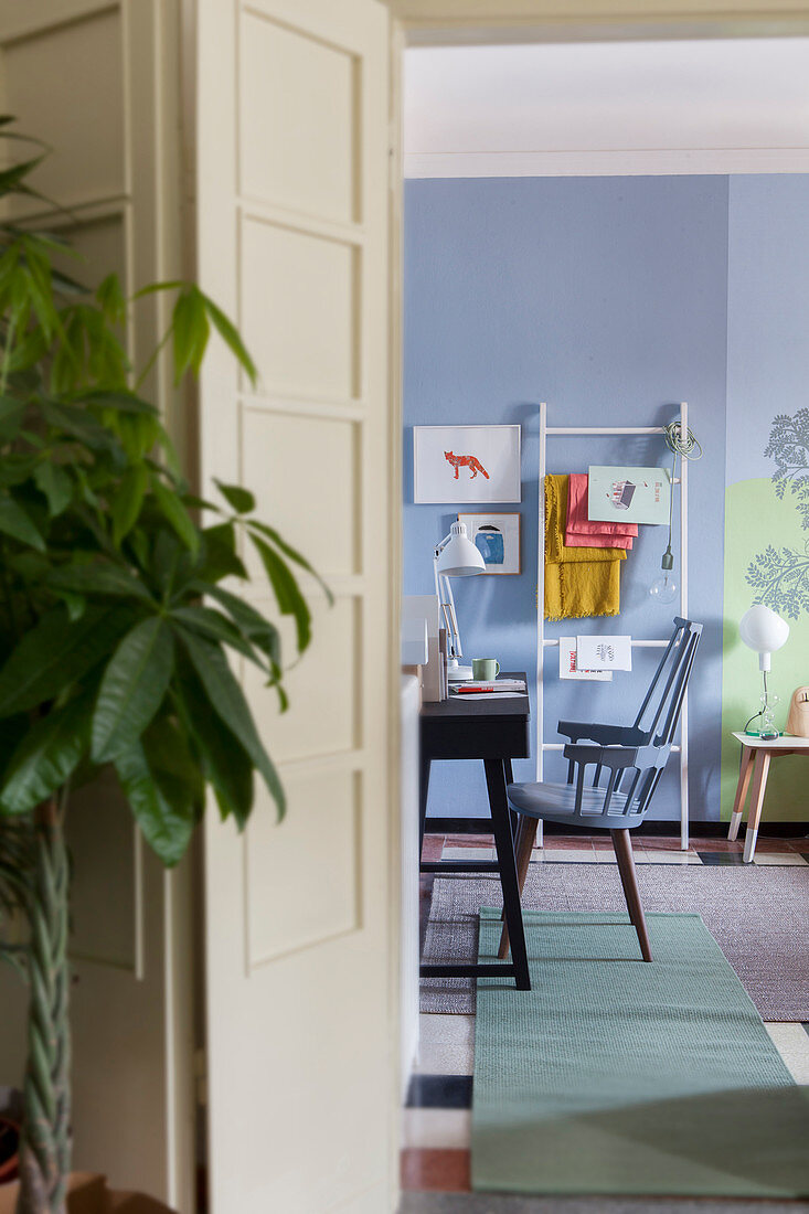 Blick durch Falttür in blau-grünen Wohnraum mit Schreibtisch und Leiterregal für Magazine