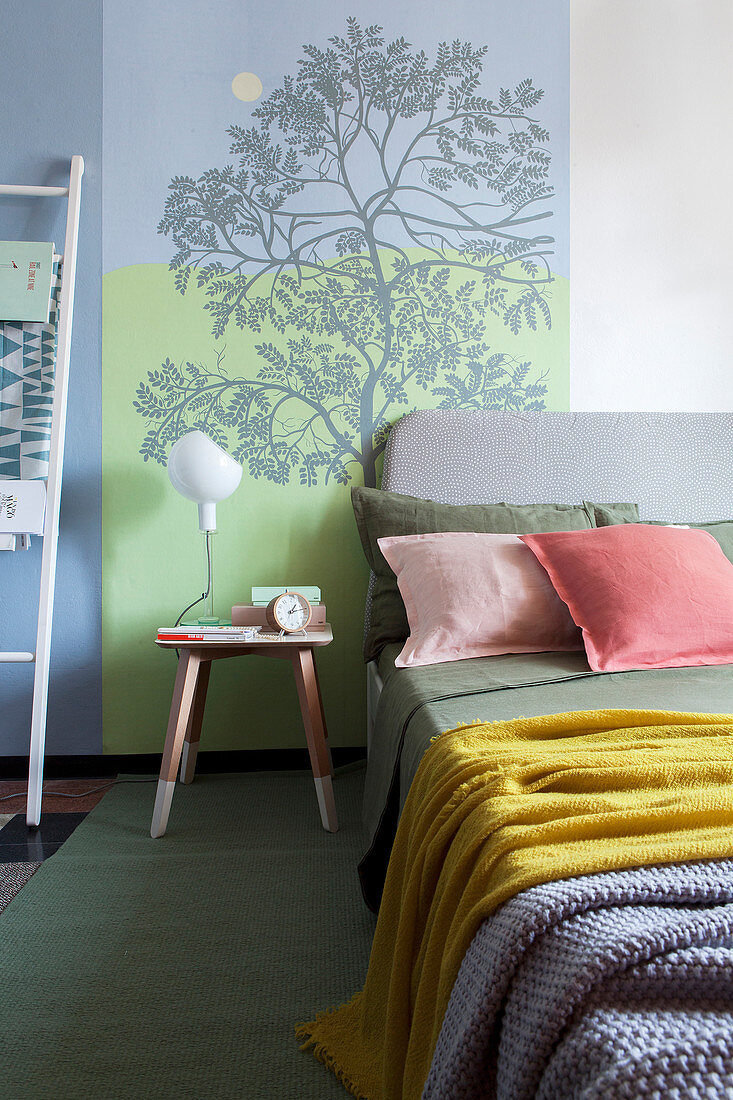 Bett und Nachttischchen vor Wand mit selbstgemaltem Baummotiv
