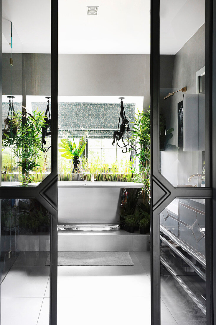 Many houseplants in bathroom seen through open, sliding glass doors