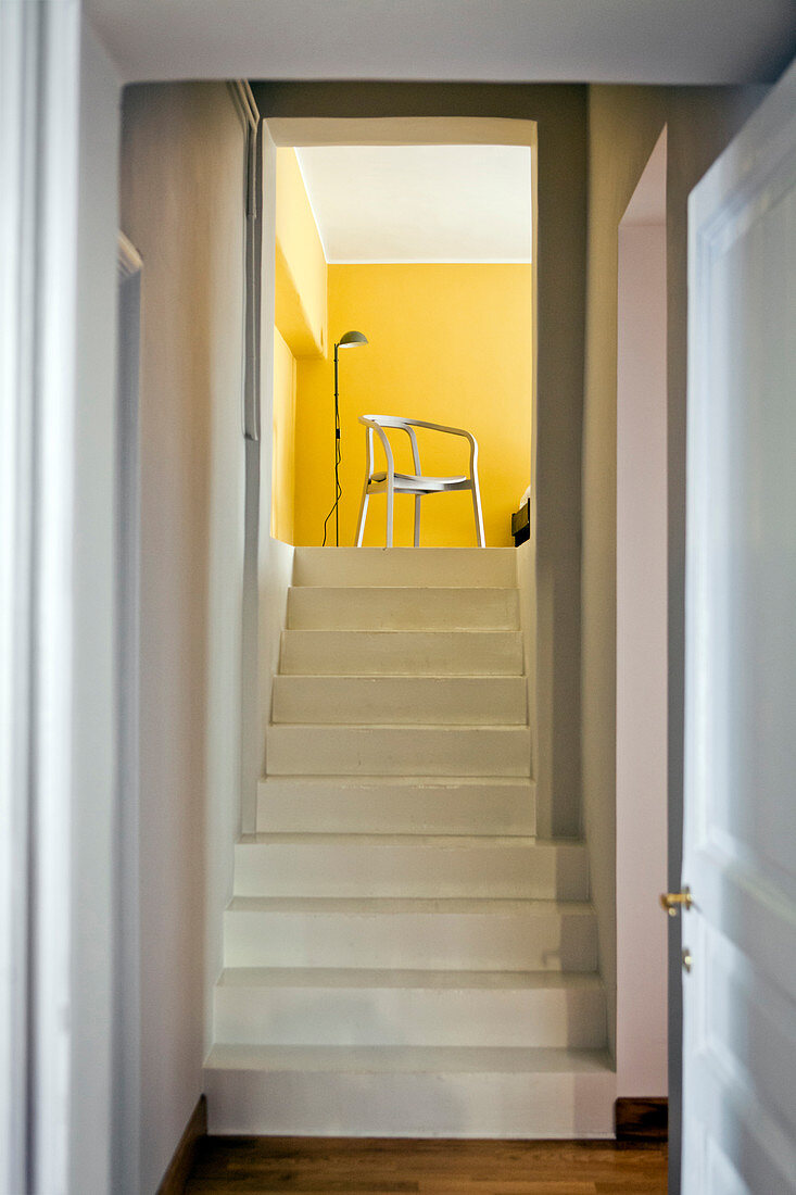 Schlichter weißer Treppenaufgang zu Wohnraum mit sonnengelben Wänden
