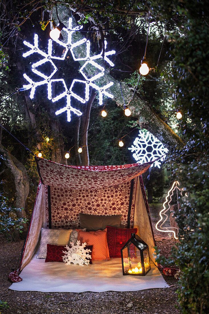 Zelt mit Kissen und Laterne im Garten mit Schneeflocken und Lichterkette dekoriertem