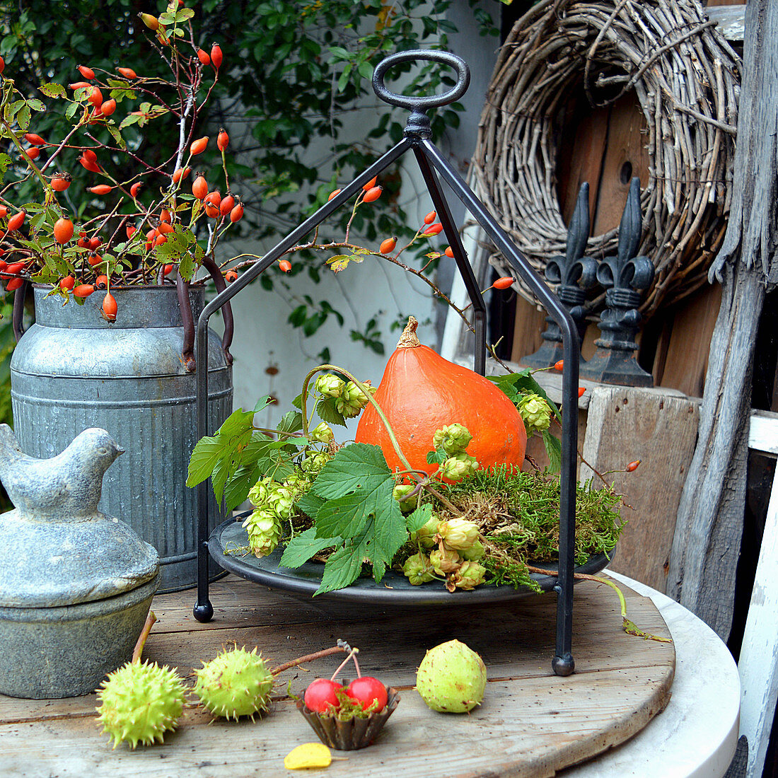 Herbstdeko mit Kürbis, Hagebutten, Hopfenranke und Kastanien