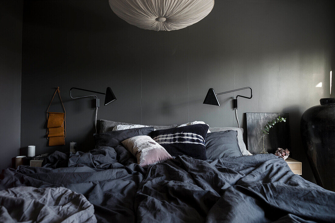 Bed with dark bed linen below lamps mounted on grey wall