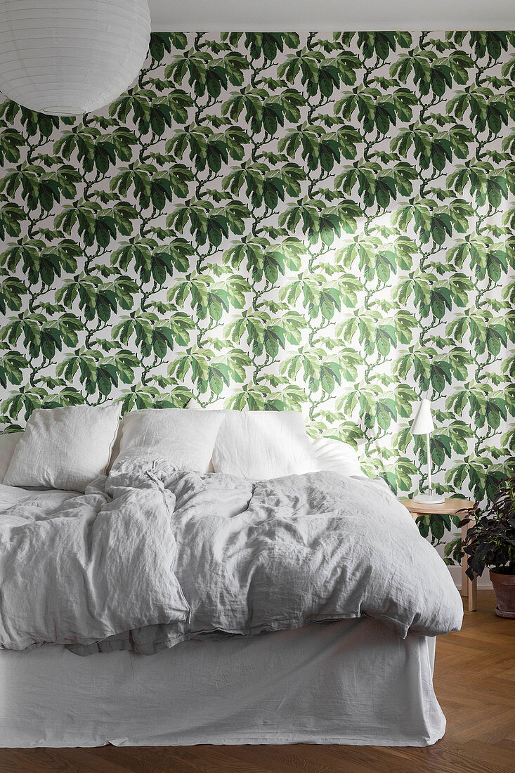 White bed with valance against leaf-patterned wallpaper in bedroom